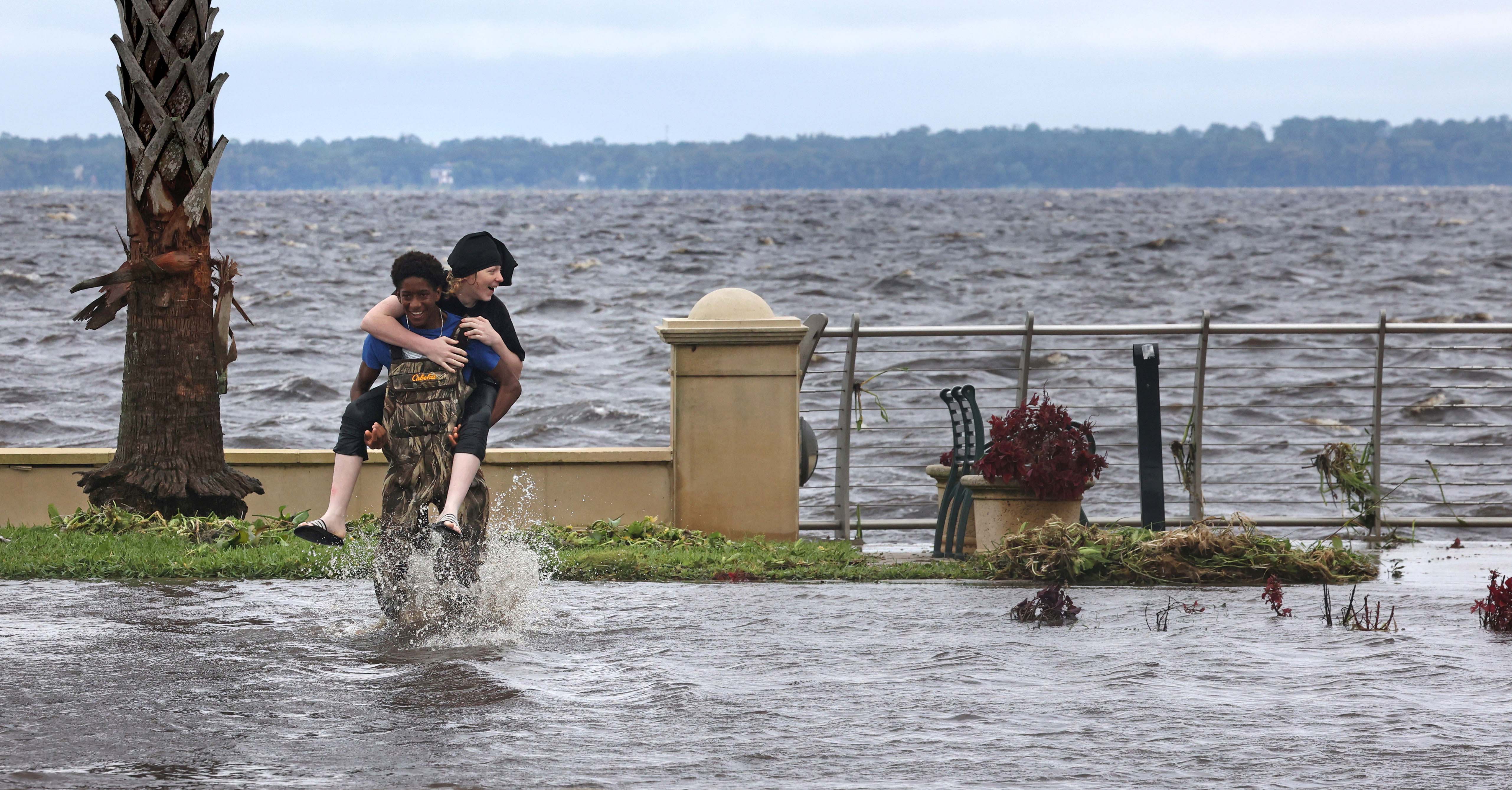 Una persona recibe un paseo en piggyback de un amigo a través de un Seminole Boulevard inundado en el centro de Sanford el 10 de octubre de 2024. Gran parte del camino que frontal el lago Monroe se inundó como resultado del impacto durante la noche del huracán Milton en el área. (Joe Burbank/Orlando Sentinel)