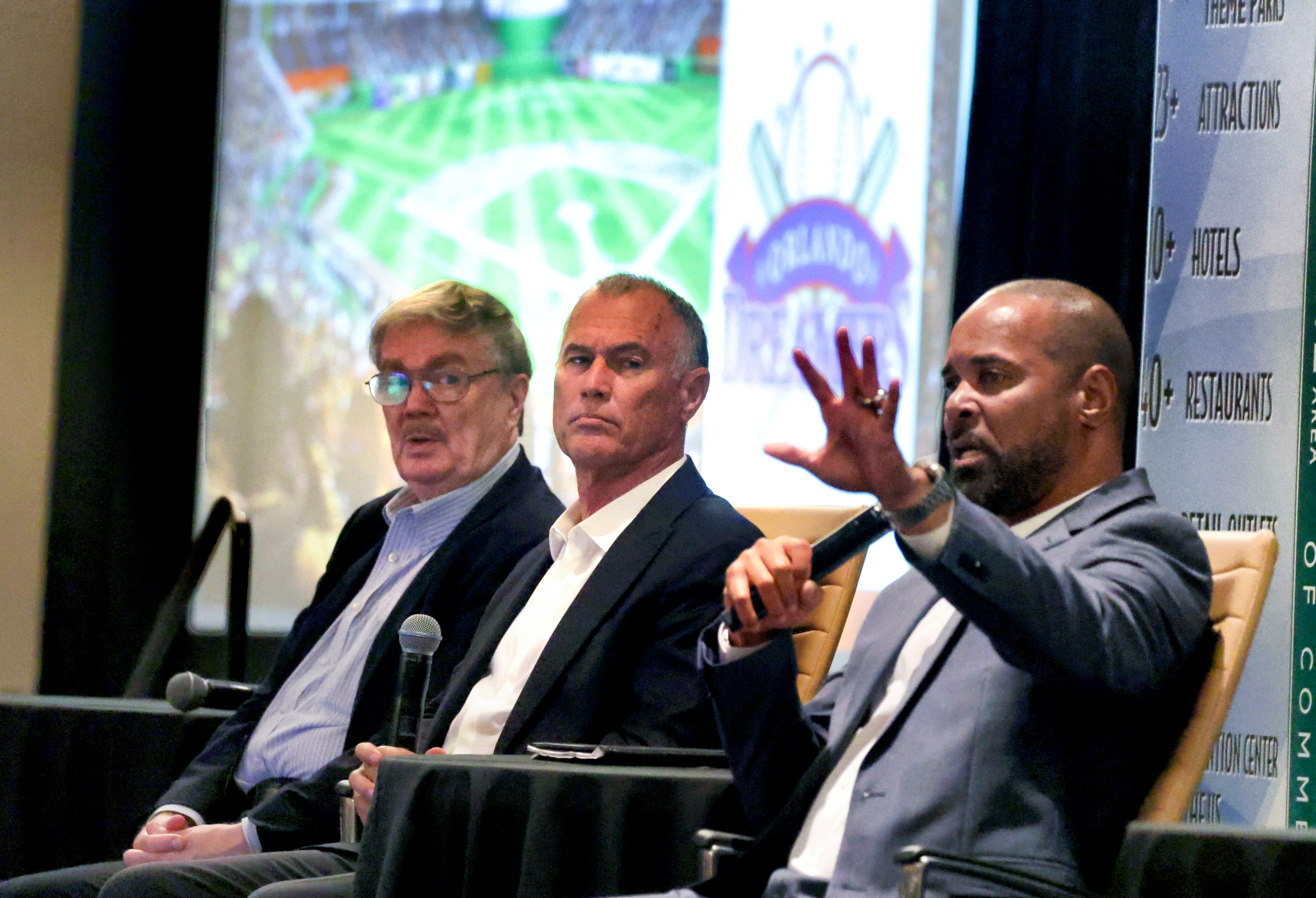 Miembros del grupo de propiedad de Orlando Dreamers MLB, Jim Schnorf, Left y el Dr. Rick Workman, escuchan el jugador del Salón de la Fama de MLB Barry Larkin, a la derecha, respondiendo una pregunta durante su presentación a la Cámara de Comercio del Área de I-Drive Resort en el Hilton Orlando, lunes 16 de junio de 2025 (Joe Burbank/Orlando Sentinel)