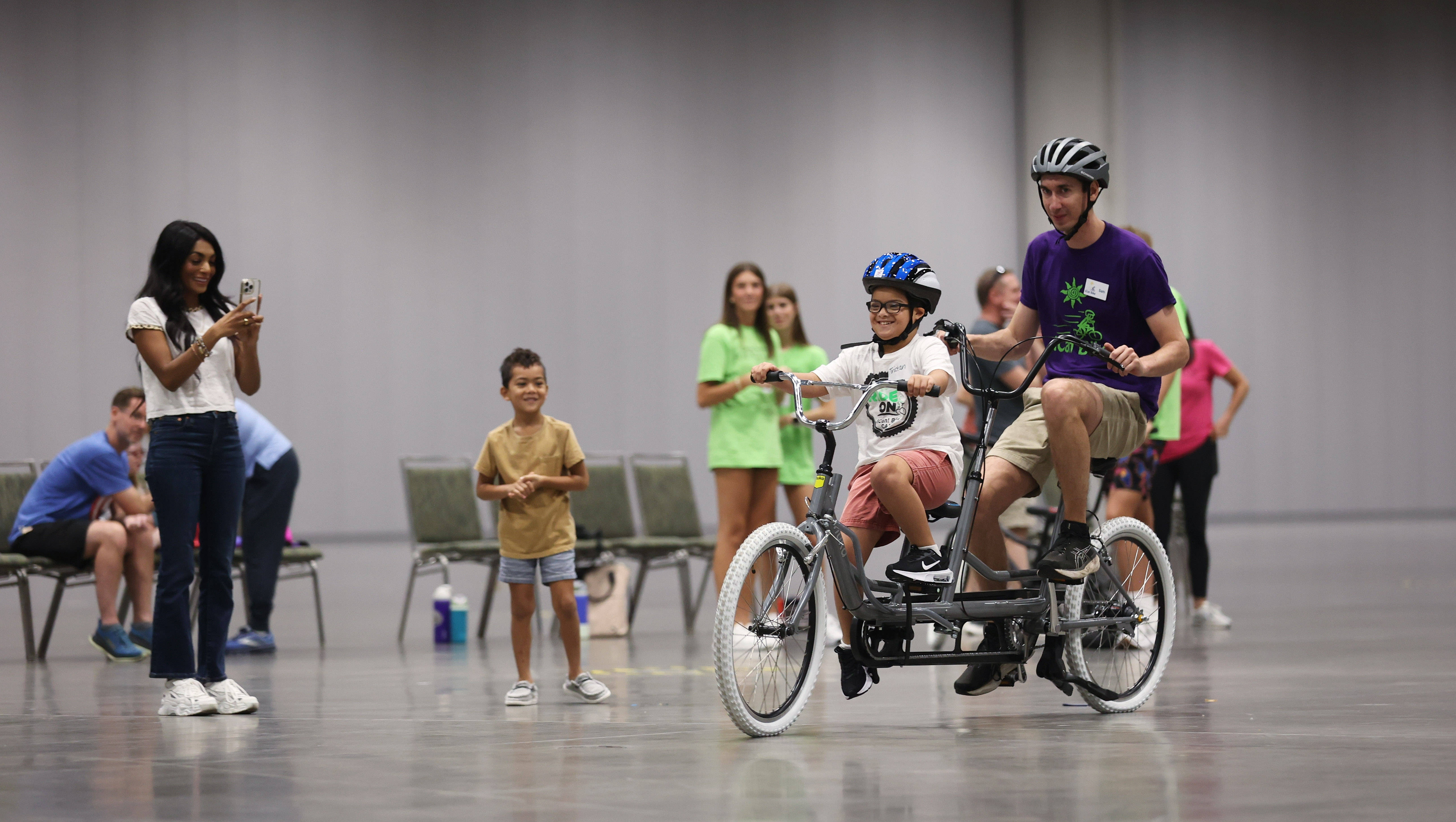 Tristan McMillen, de 8 años, monta una bicicleta tándem con Ican Bike Bike Tech Sam Marcucci cuando la Fundación del Síndrome de Down de Florida alberga un ICAN! Campamento de bicicletas en el Centro de Convenciones del Condado de Orange, el martes 22 de julio de 2025. (Ricardo Ramirez Buxeda/Orlando Sentinel)