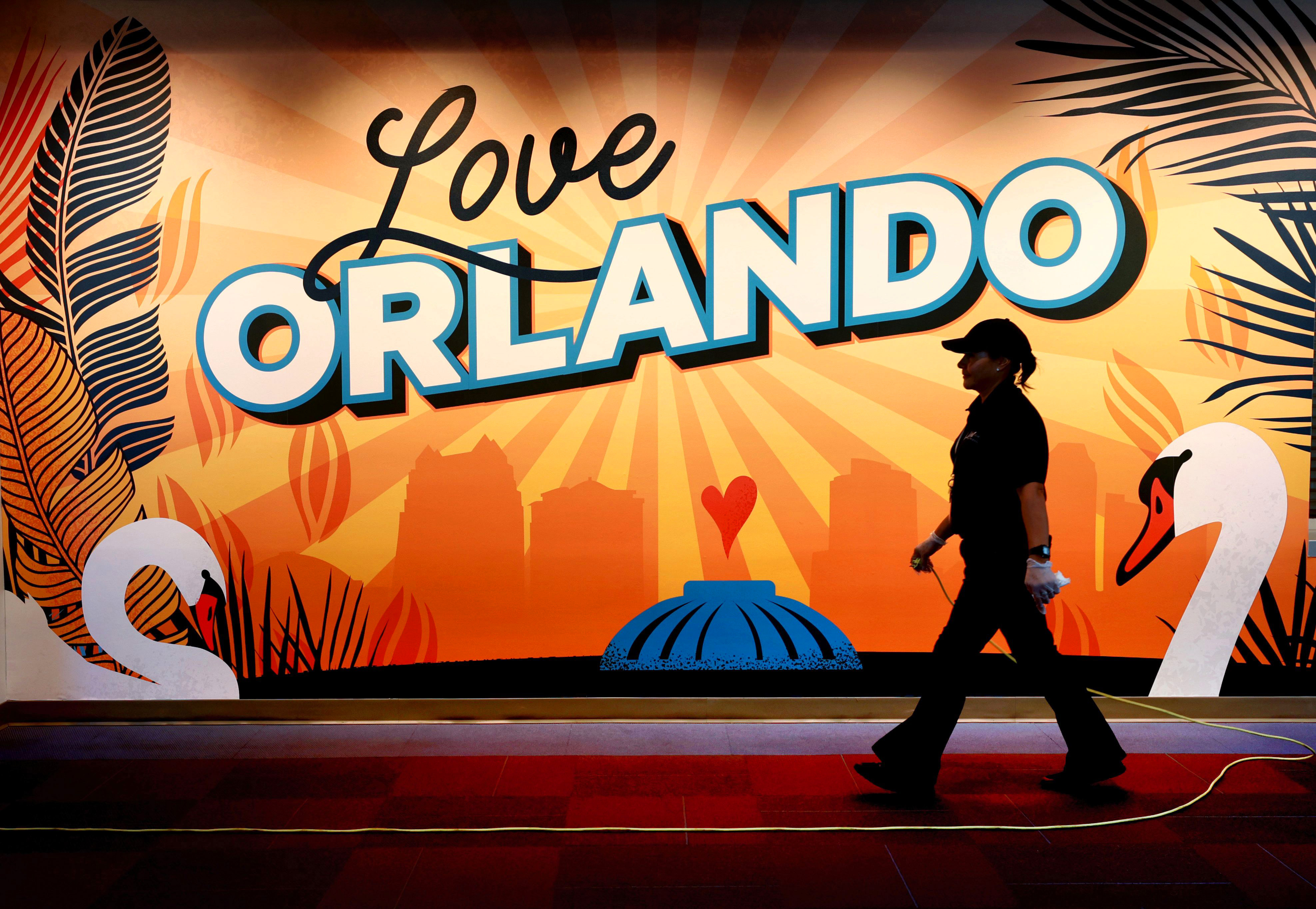 LOVING ORLANDO – El mural en la entrada este del puente peatonal del tercer piso en CNL Center City Commons en el centro de Orlando ofrece un colorido telón de fondo para un trabajador de limpieza, el viernes 9 de junio de 2023. City Commons consta de las dos torres de oficinas de CNL, el Ayuntamiento de Orlando y el estacionamiento adyacente, con numerosos proyectos de arte en exhibición en todo el complejo. (Joe Burbank/Orlando Sentinel)