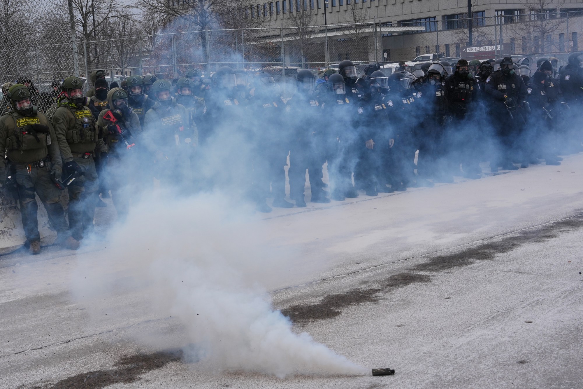 Oficiales federales de inmigración se encuentran frente al edificio federal Bishop Henry Whipple mientras se lanzan gases lacrimógenos el jueves 15 de enero de 2026 en Minneapolis. (Foto AP/Adam Gray)