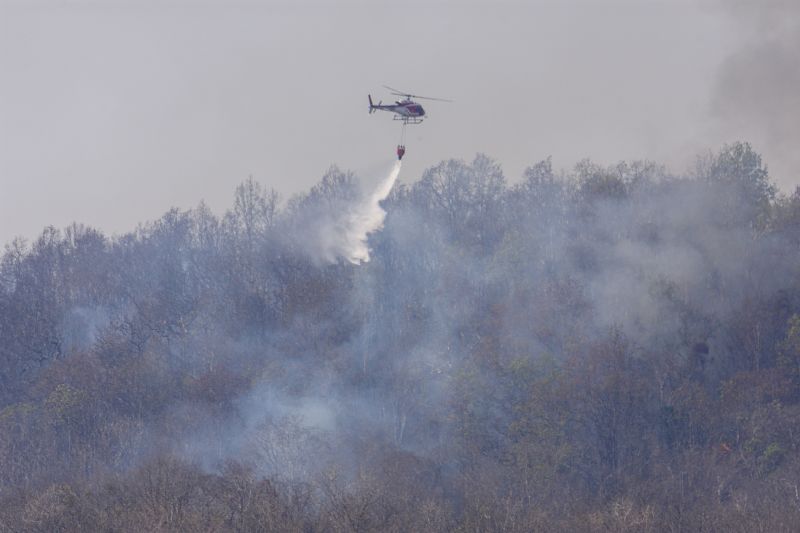 Helicóptero arrojando agua sobre un incendio forestal en terreno accidentado.