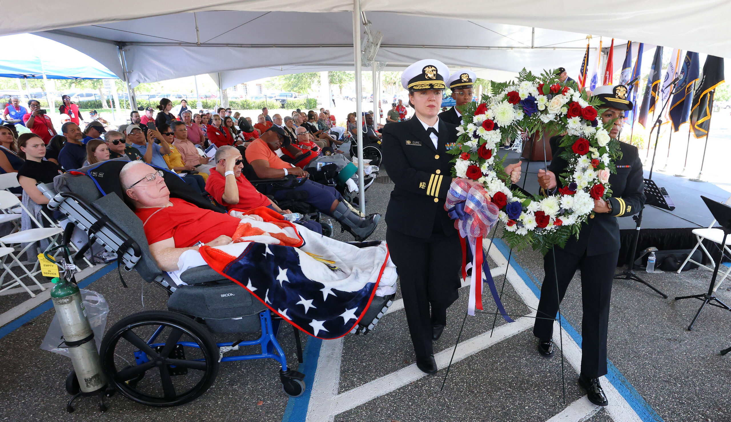 HONRANDO A LOS VETERANOS Duane Hunt, veterano de infantería del ejército de EE. UU., izquierda, observa cómo miembros del Servicio de Salud Pública de EE. UU. presentan una corona de flores durante la ceremonia del Día de los Caídos en el Centro Médico VA de Orlando en Lake Nona, el viernes 23 de mayo de 2025. Hunt sirvió tres años en Vietnam. Líderes militares y funcionarios electos se reunieron en el VA para la ceremonia con varios cientos de veteranos para dar inicio al fin de semana del Día de los Caídos. (Joe Burbank/Orlando Sentinel)