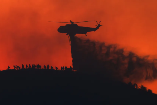Un avión cisterna arroja agua mientras bomberos caminan debajo, mientras el incendio Sandy Fire se aproxima el martes 19 de mayo en Simi Valley, California.